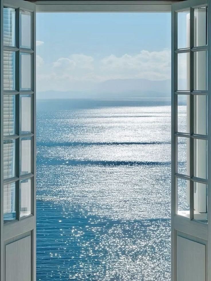 Ventana abierta con vista al mar Mediterráneo, luz brillando sobre el agua